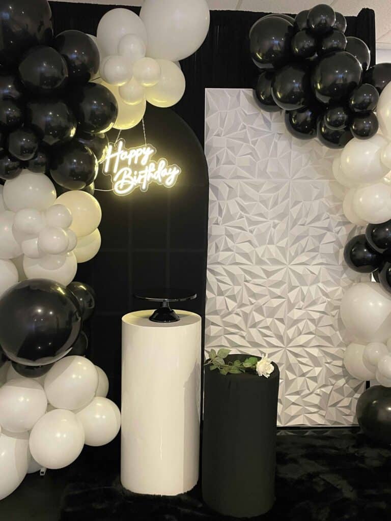 Black and white balloon garland with a neon Happy Birthday sign and floral wall
